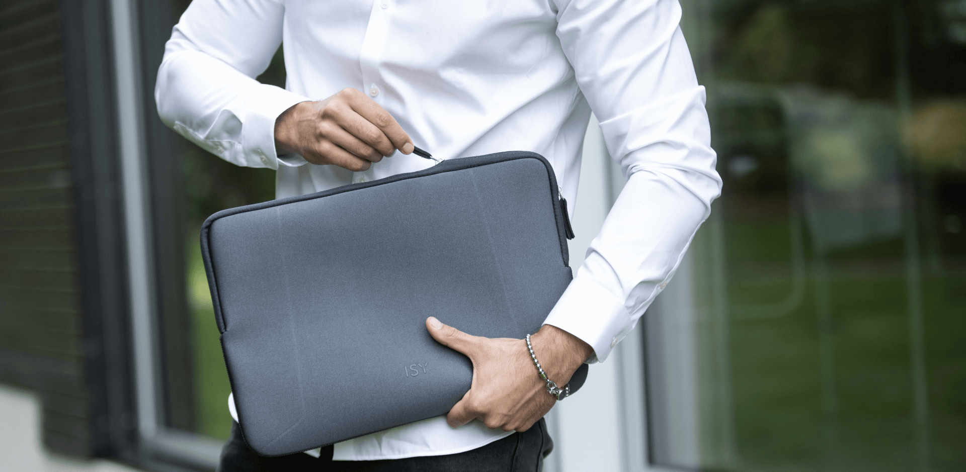 Jonge man met wit hemd houdt een laptoptas van het merk ISY vast, in de natuur, close-upbeeld