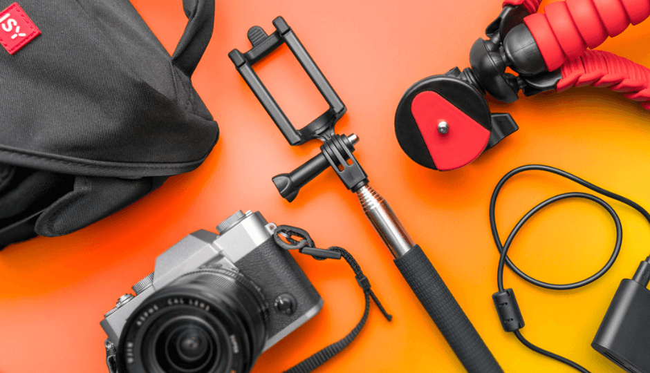 Vista superior de productos fotográficos de la marca ISY, entre ellos un palo selfie, un trípode, funda para la cámara y cable de carga de la marca ISY, en corte